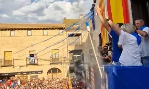 Gente celebra las fiestas de Utebo, ondeando banderas y lanzando confeti desde un balcón.