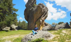 Mujer sentada en roca, con imponente formación rocosa detrás. Un paisaje natural que demuestra que merece la pena visitar Soria.