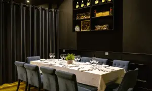 Mesa elegante con sillas azules y mantel blanco, lista para el menú del día de la buganvilla. Botellas de vino en estantería.