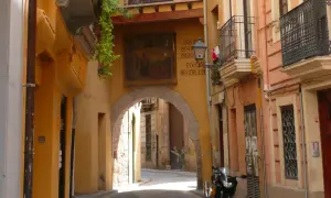 Calle estrecha con arco, fachadas amarillas y naranjas, un balcón y una moto. Descubre los **secret places Valencia**.