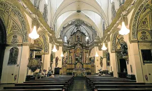 Interior de la iglesia de la Magdalena en Zaragoza, con bancos de madera, un retablo dorado y esculturas.