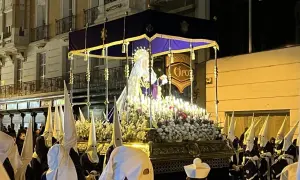 Procesión del Santo Entierro en Zaragoza. Figuras religiosas iluminadas por velas, rodeadas de nazarenos con túnicas y capirotes blancos.