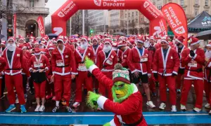 Multitud de personas disfrazadas de Papá Noel en Zaragoza, listas para una carrera. Un Grinch verde se une a la fiesta.