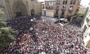 Multitud celebra en la plaza de Huesca, con globos verdes y blancos flotando. La fiesta prelaurentis inunda las calles.