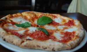 Pizza margarita recién horneada, con tomate y mozzarella fundida, decorada con hojas de albahaca fresca. ¡Una delicia que te hará buscar las mejores pizzerías Zaragoza!