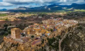 Pueblo blanco en un acantilado con castillo, ideal para saber qué ver en Murcia y alrededores. Paisaje montañoso al fondo.
