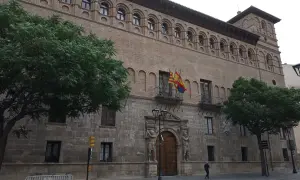 Fachada del palacio de los Luna en Zaragoza, con sus arcos y balcones, flanqueado por árboles verdes.