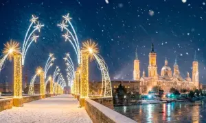 Puente nevado con encendido luces navidad Zaragoza. La Basílica del Pilar brilla bajo la nieve.