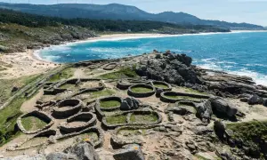 Ruinas circulares de un castro gallego, un lugar histórico que ver en A Coruña, con el mar azul y la costa de fondo.