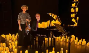 Músicos disfrutan de un concierto con velas. Una violinista y un pianista posan junto a un piano rodeado de velas encendidas.