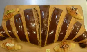 Un croissant gigante con glaseado de chocolate y pequeños croissants decorados, perfectos para un desayuno en Zaragoza.