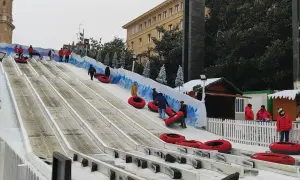 Diversión en los trineos de la Plaza del Pilar. Niños y adultos disfrutan de un tobogán nevado, con la Basílica de Nuestra Señora del Pilar de fondo.