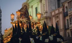 Figuras encapuchadas portan un paso con la Virgen, iluminado por velas, durante las procesiones de Sábado Santo.