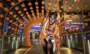 Un espeluznante zombie con maquillaje de Halloween avanza bajo un arco decorado con calabazas en Puerto Venecia.