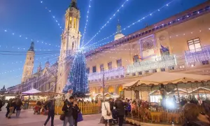 Mercado navideño en Zaragoza con árbol iluminado y gente paseando. Descubre qué ver en Zaragoza en Navidad.