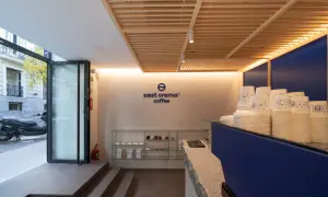 Interior de cafetería con logo "east crema coffee", vasos apilados y estanterías con productos.