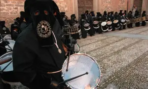 Tambores resuenan en las procesiones de Zaragoza. Nazarenos con túnicas negras y capirotes golpean sus tambores, creando un ritmo solemne.