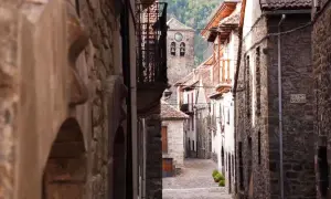 Calle empedrada en un pueblo de Aragón, con casas de piedra y un campanario al fondo.