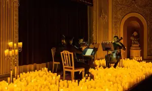 Un concierto de música clásica bajo la luz de miles de velas en Zaragoza. Músicos tocan violines y violonchelos en un escenario iluminado por velas.