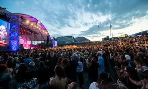 Multitud disfrutando de un concierto al aire libre. Se ve un gran escenario con luces y pantallas, y miles de personas animando. ¡Así se vive latino Zaragoza!