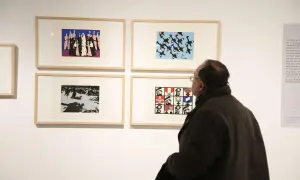 Un hombre observa obras de arte en una galería, incluyendo una que representa figuras militares y banderas, evocando el estilo de Pablo Serrano.