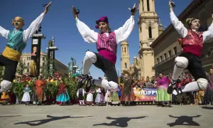 Jóvenes bailan jotas del Pilar con castañuelas, saltando enérgicamente. Al fondo, gente vestida de época y edificios históricos.