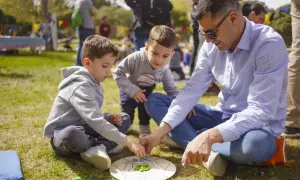 Un padre y sus hijos disfrutan de un juego en el césped, creando un momento familiar entre las tribus del parque Zaragoza.