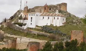 Iglesia Nuestra Señora de Gracia, un edificio blanco con tejado a dos aguas, se alza en una colina rocosa junto a ruinas de un castillo.