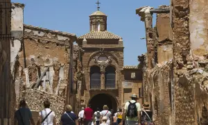 Gente camina por las ruinas de Belchite Viejo, un pueblo fantasma con edificios derruidos y una iglesia en el centro.