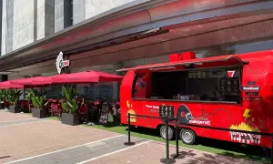 Food truck rojo "Puro Goxis" de Dabiz Muñoz, con "Mamma!!!" y "Alta cocina callejera!!" escrito. Mesas y sombrillas rojas al lado.