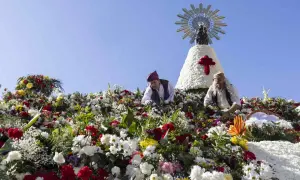 Ofrenda de flores a la Virgen del Pilar. Hombres colocan flores en una estructura adornada con la imagen de la Virgen.