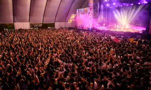 Multitud vibrante en concierto, con luces de escenario y carteles. Se aprecia la **autorización menores espacio Zity** en un cartel.