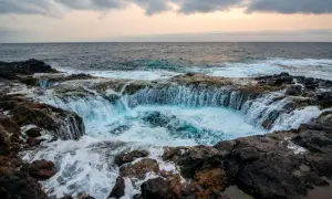 El mar choca contra las rocas volcánicas, creando una cascada de agua azul en un agujero natural. Un lugar impresionante que ver en Gran Canaria.