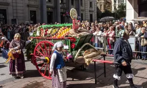 Carro con ofrenda de frutos, pan y verduras, adornado con flores, desfila entre una multitud.