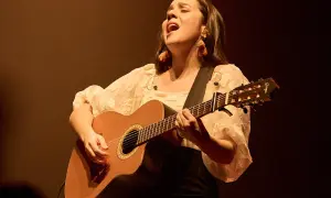 Valeria Castro Zaragoza canta con pasión, guitarra en mano, bajo una luz cálida.