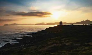 Atardecer en la costa gallega, con un faro solitario y siluetas de personas contemplando el mar. Un paisaje idílico para tus destinos Galicia.