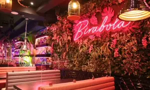 Un interior vibrante con un letrero de neón "Pirabola" sobre una pared de vegetación exuberante. Mesas y asientos de estilo cabina crean un ambiente acogedor, ideal para descubrir restaurantes originales en Zaragoza.