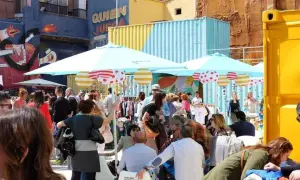 Gente comprando ropa en un animado mercadillo de las armas, con coloridos contenedores y murales de fondo.