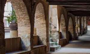 Pasaje abovedado de piedra y ladrillo con arcos, bancos de piedra y una planta en maceta. Un lugar con encanto para pasear y descubrir la fresneda que ver.