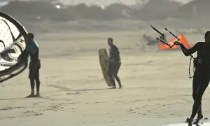 Hombres preparándose para el kitesurf en Lanzarote, con sus cometas y tablas listas para la acción en la playa.