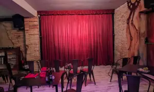 El escenario de el.sotano magico, con cortinas rojas y sillas metálicas, listo para un espectáculo.