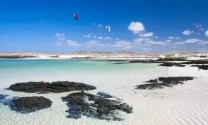 Aguas turquesas y arena blanca en Fuerteventura, con kitesurfistas en el horizonte. Un paraíso entre los 10 sitios para visitar en Fuerteventura.
