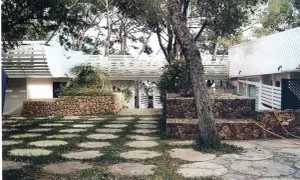 La casa Huarte, rodeada de árboles, presenta un patio con círculos de piedra y césped, muros de piedra y un diseño arquitectónico moderno.