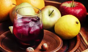 Un refrescante tinto de verano con espuma de limón, rodeado de frutas frescas como naranjas, manzanas y un limón amarillo.
