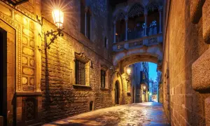Calle empedrada y húmeda bajo un puente gótico iluminado, un rincón de los secret places Barcelona.
