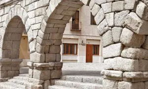 Arcos de piedra del Acueducto de Segovia, un lugar imprescindible que ver en Segovia. Al fondo, la fachada de un edificio con el letrero "El Silencio".