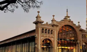 El **mercado central Zaragoza** con su arquitectura de hierro y cristal, iluminado al atardecer. Gente pasea por la entrada principal.