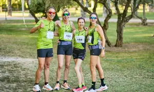 Cuatro corredores sonríen, listos para las carreras populares Zaragoza. Llevan camisetas verdes con dorsales y gafas de sol.