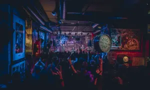 Una banda toca rock y blues en un local con luces de neón. El público levanta las manos, creando una atmósfera vibrante, como si estuvieran en una gran casa en Zaragoza.