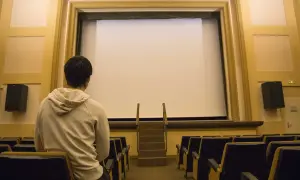Un joven espera en un cine vacío, listo para disfrutar de una película.